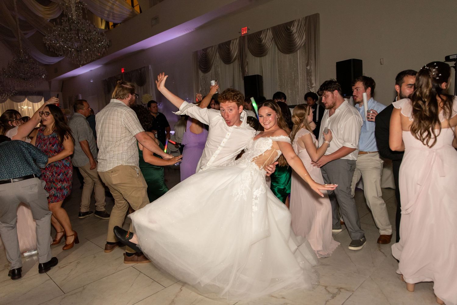 Bride and groom dancing joyfully with wedding guests on a decorated ballroom dance floor.