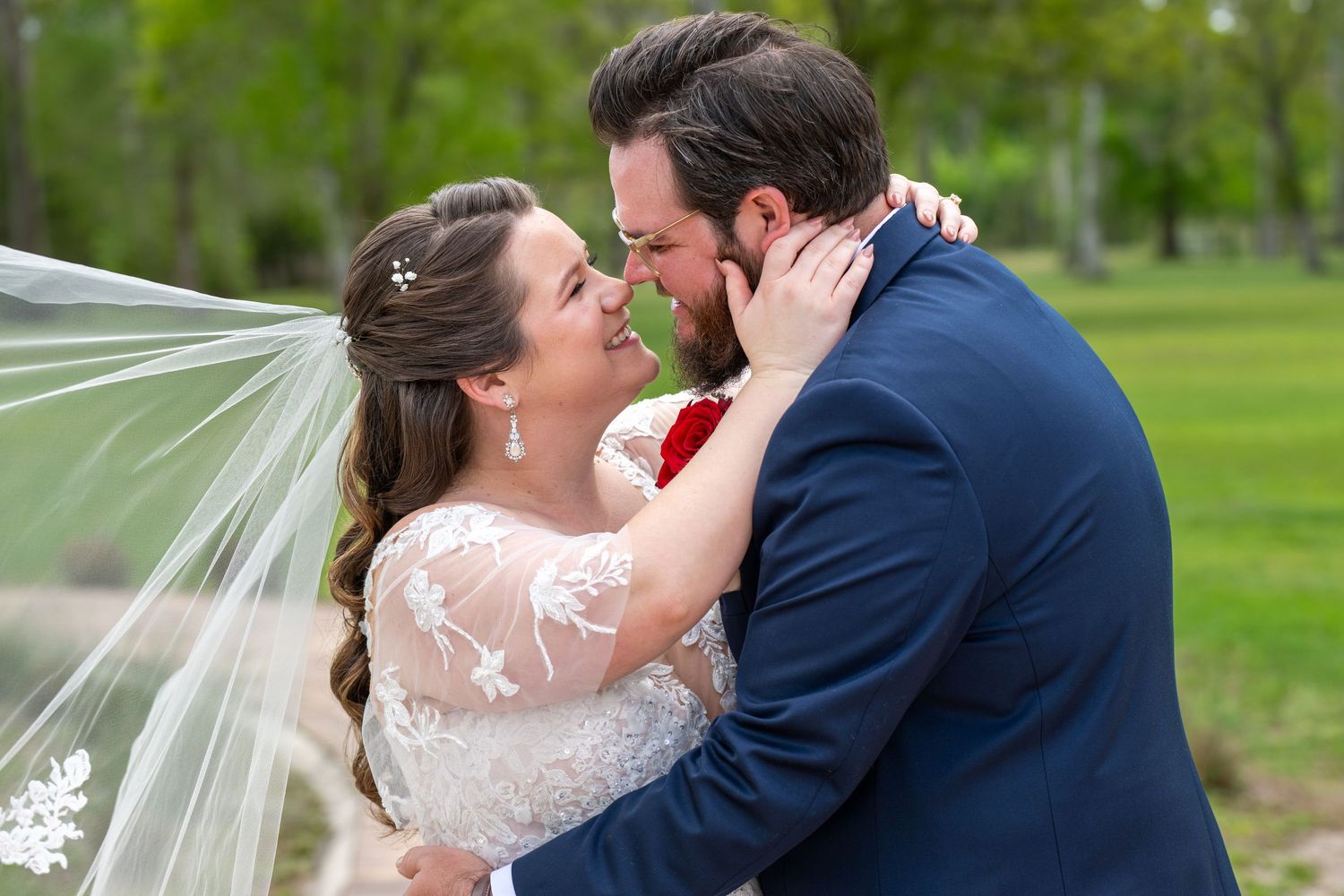 Bride and groom lean in for a kiss under a flowing veil in a scenic outdoor spring setting.