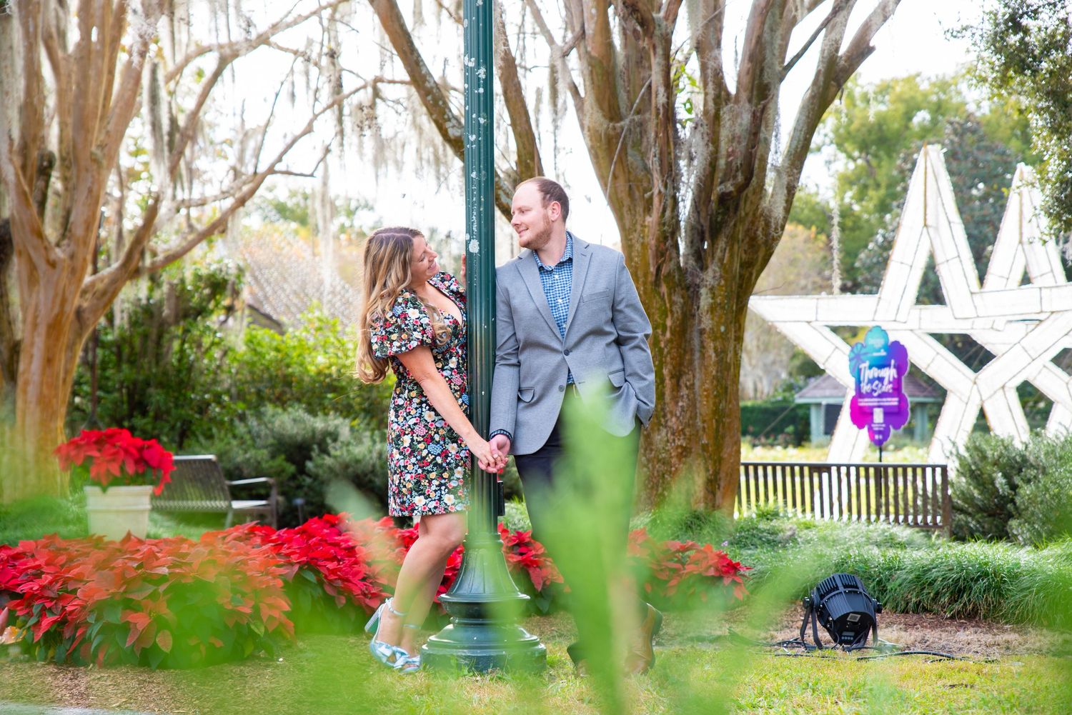 Happy couple holding hands and smiling at each other in a colorful garden park setting.