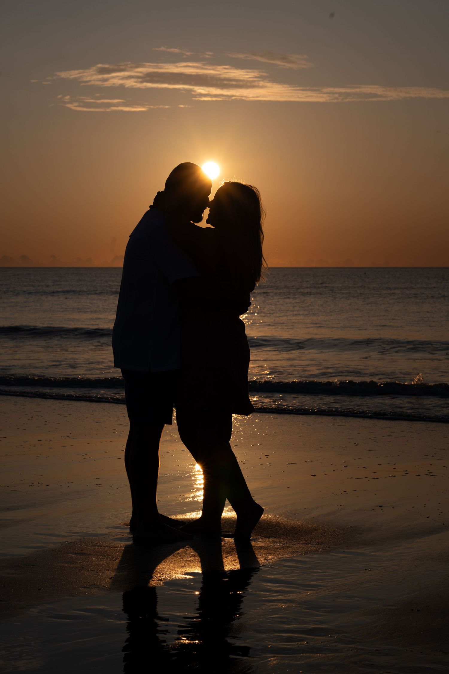 Romantic couple silhouetted against a golden sunset on a beach, sharing an intimate moment by the ocean.