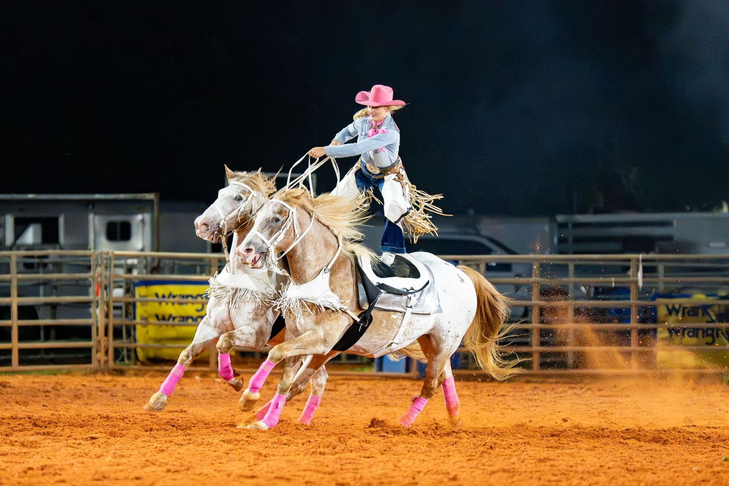 A cowgirl on a palomino horse competes in a barrel racing event at a night rodeo.