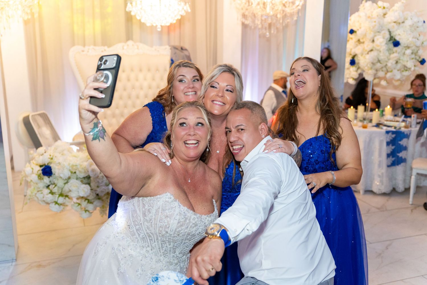Bride and bridesmaids in blue dresses take a fun group selfie at a elegant wedding reception venue.