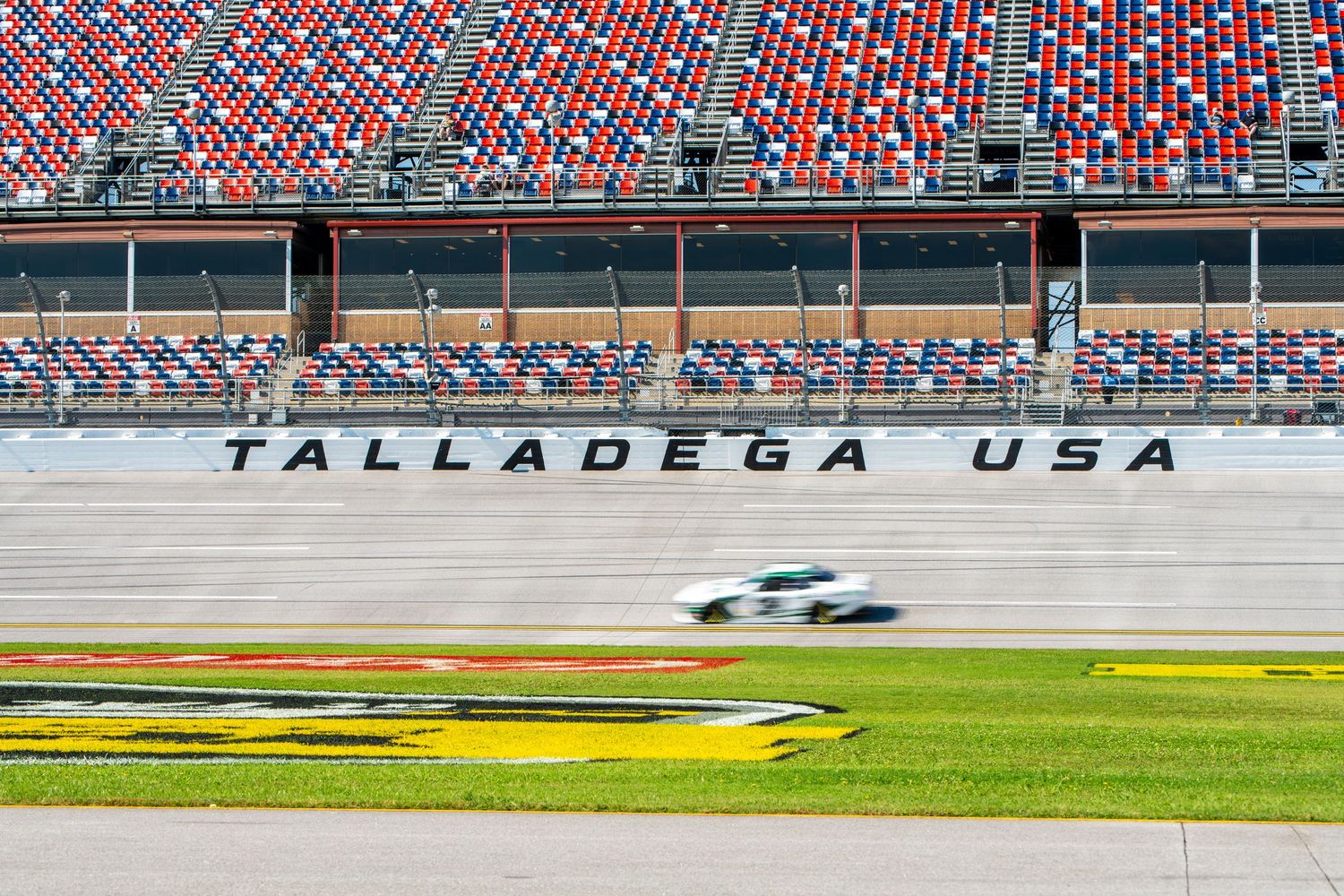 NASCAR race car blurs past iconic Talladega USA grandstand lettering on superspeedway.