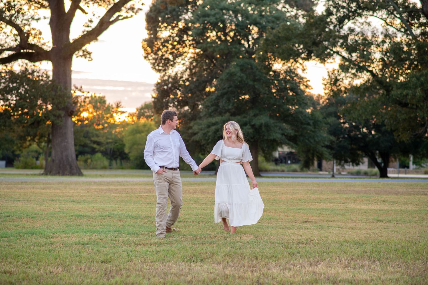 Happy couple holding hands and dancing in an open field during a warm golden sunset.