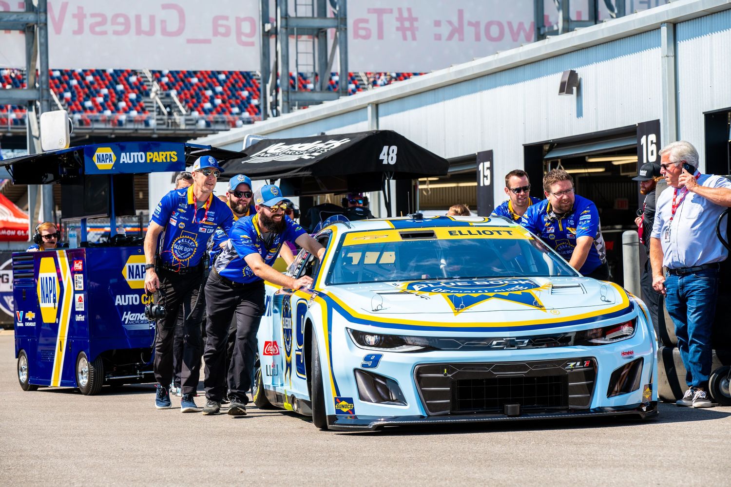 NASCAR pit crew pushing the NAPA Auto Parts number 48 Chevrolet Camaro through the garage.