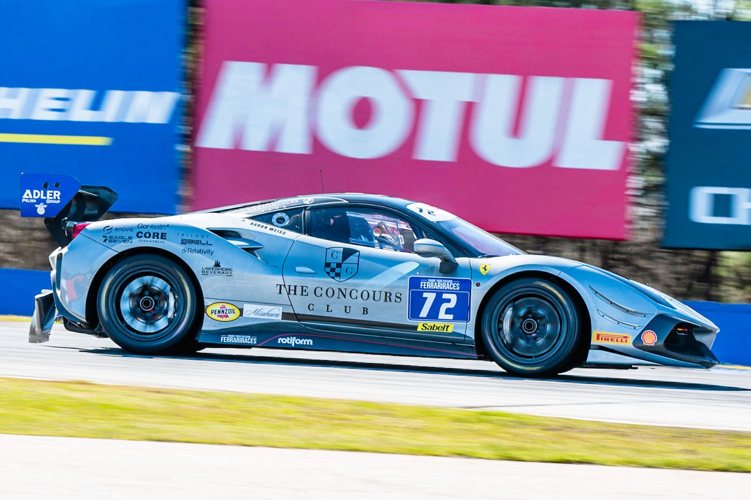 Silver Ferrari 488 GT3 number 72 with Concours livery racing past Motul signage.