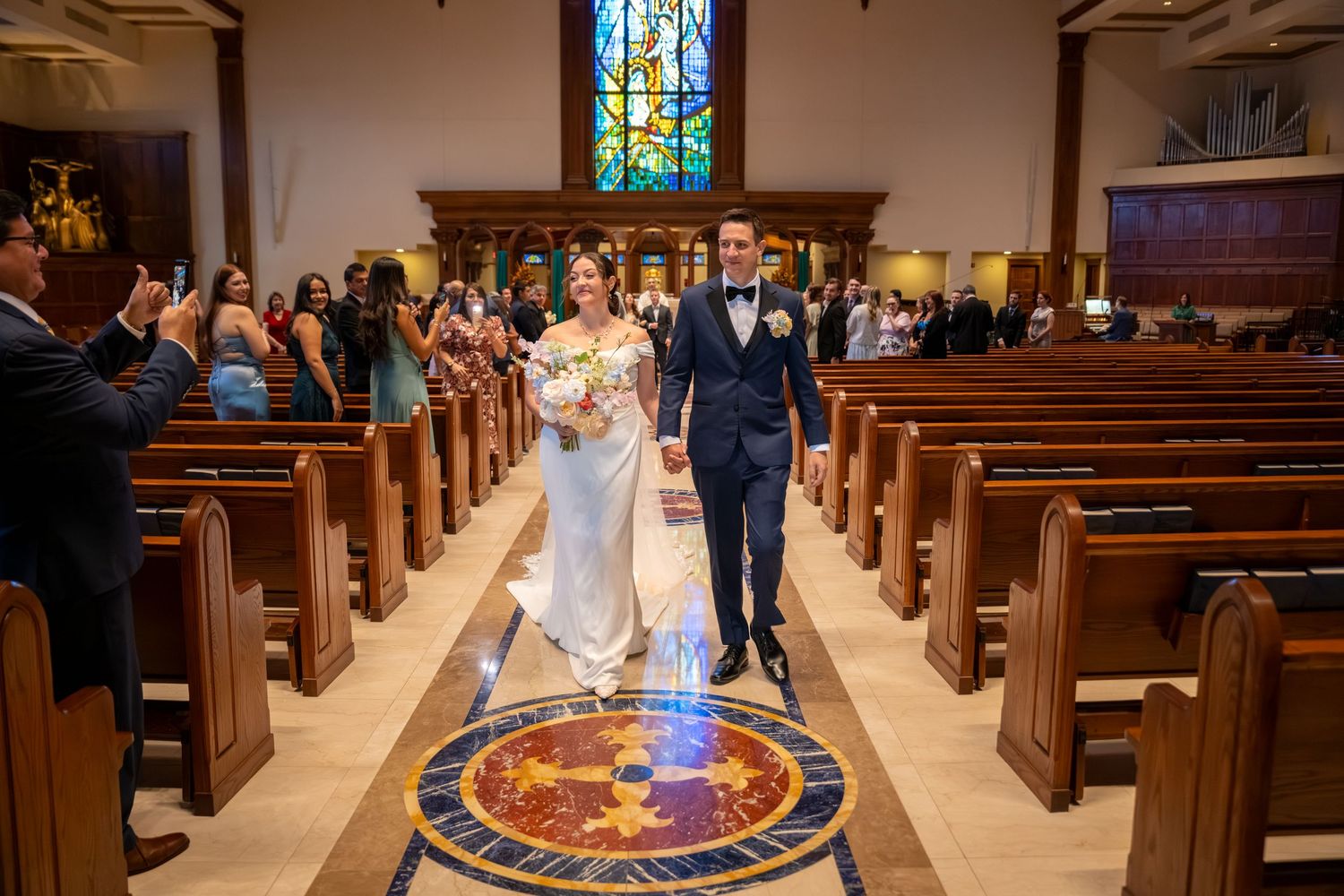 Newlyweds walking joyfully down the aisle of a beautiful church with stained glass windows after ceremony.