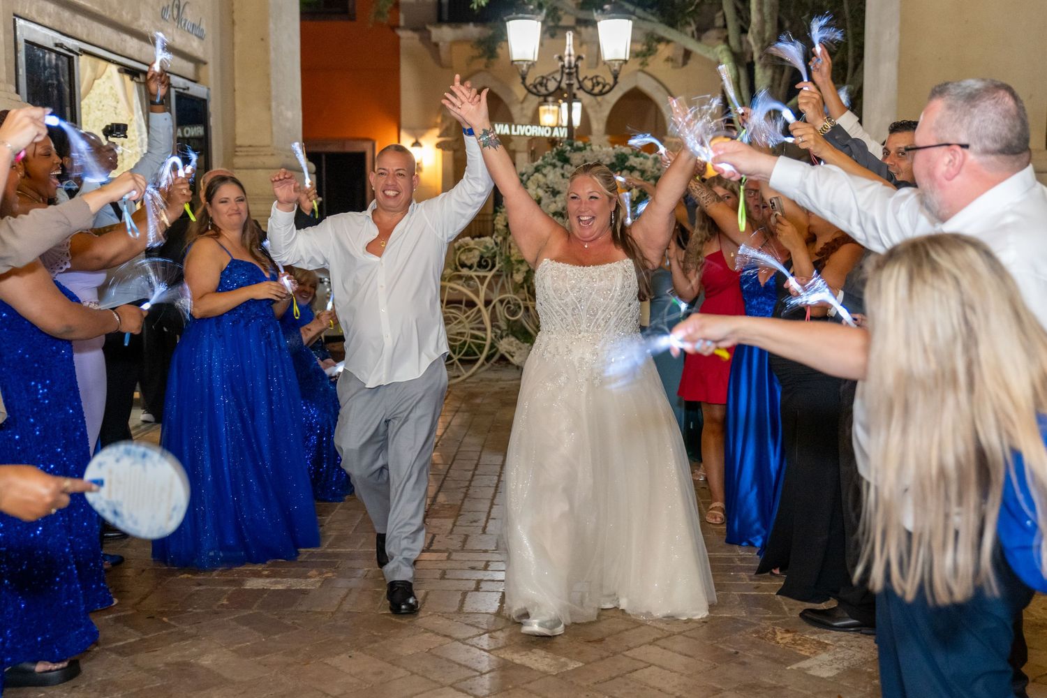 Bride and groom celebrate wedding exit through sparkler tunnel with guests in royal blue attire at elegant venue.