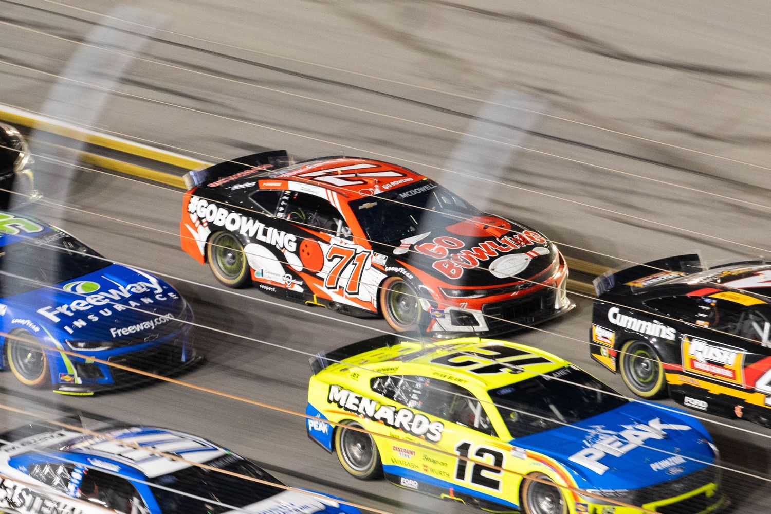 NASCAR cars colliding in a multi-car crash at a nighttime superspeedway race.