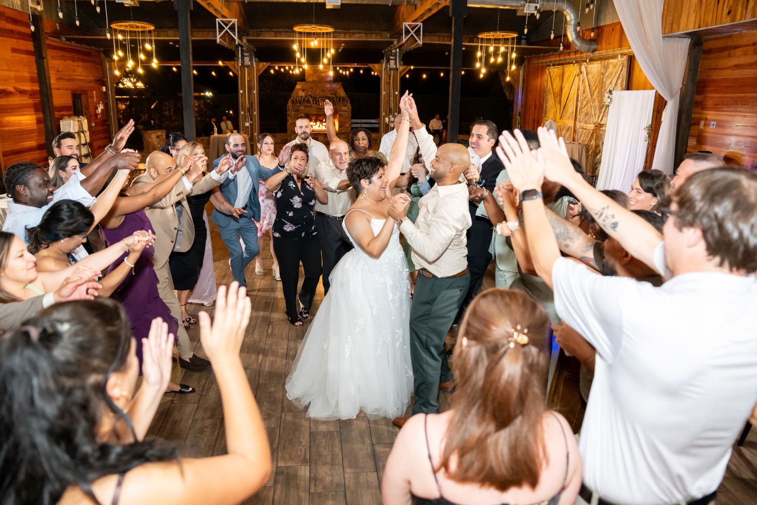 Bride and groom share joyful grand exit with guests raising hands in rustic wedding reception venue.