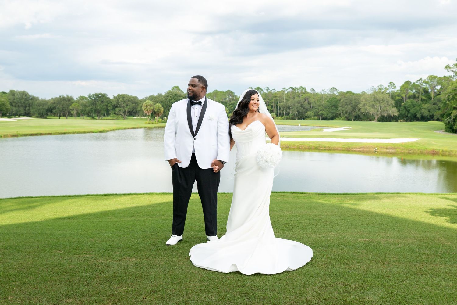 Bride and groom pose on lush golf course green with pond backdrop on their wedding day.