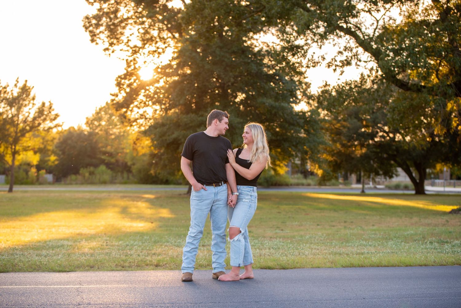 Couple holding hands and smiling at each other during a golden hour outdoor engagement session.