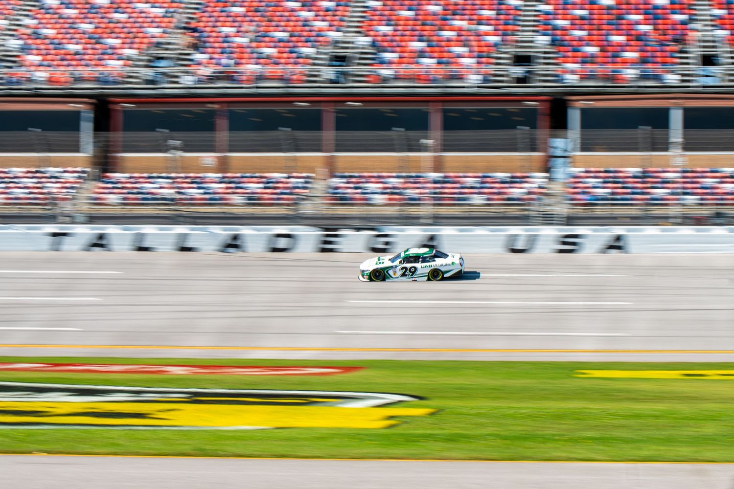 Race car speeding past Talladega USA lettering on empty grandstand superspeedway.