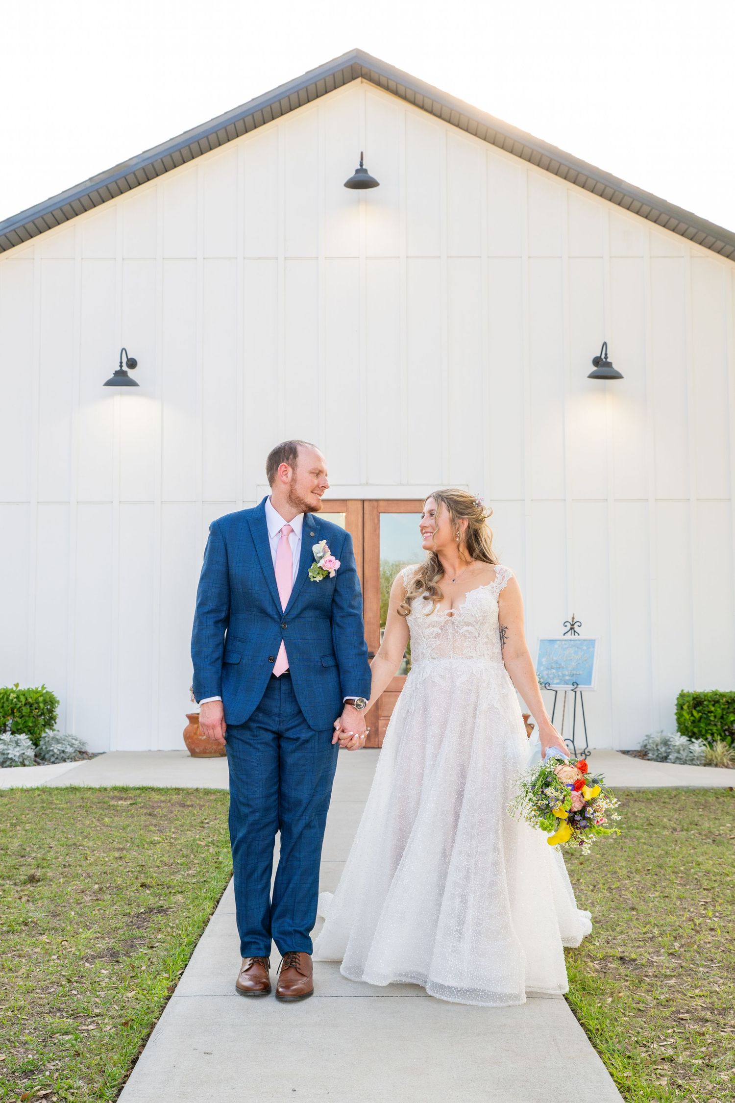 Bride and groom holding hands walking in front of white barn wedding venue.