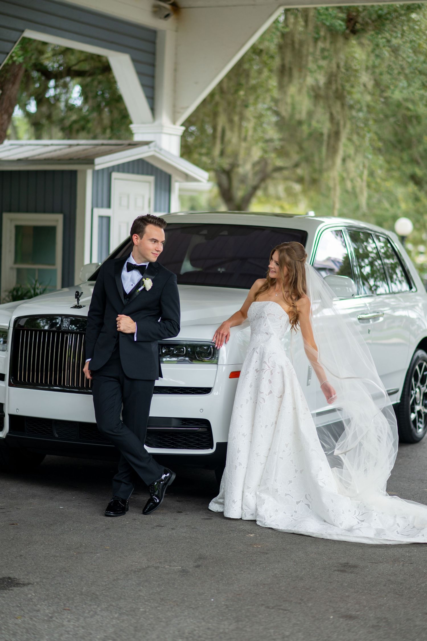 Bride and groom posing elegantly beside a white Rolls-Royce on their wedding day.