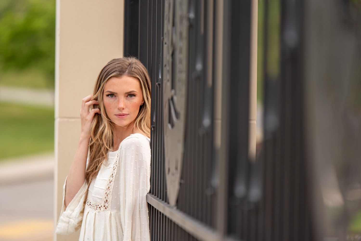 Elegant young woman in a white dress posing gracefully beside a dark metal fence outdoors.