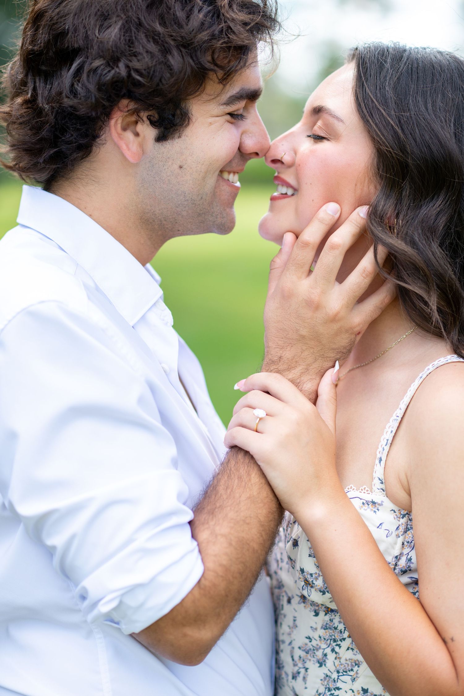 A happy couple shares a romantic moment outdoors, with the woman wearing an engagement ring.