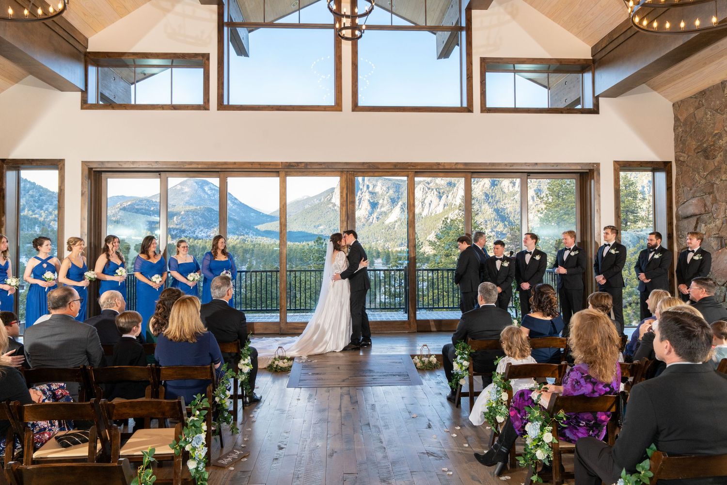 Mountain wedding ceremony in rustic venue with panoramic views, bride and groom at altar with wedding party.