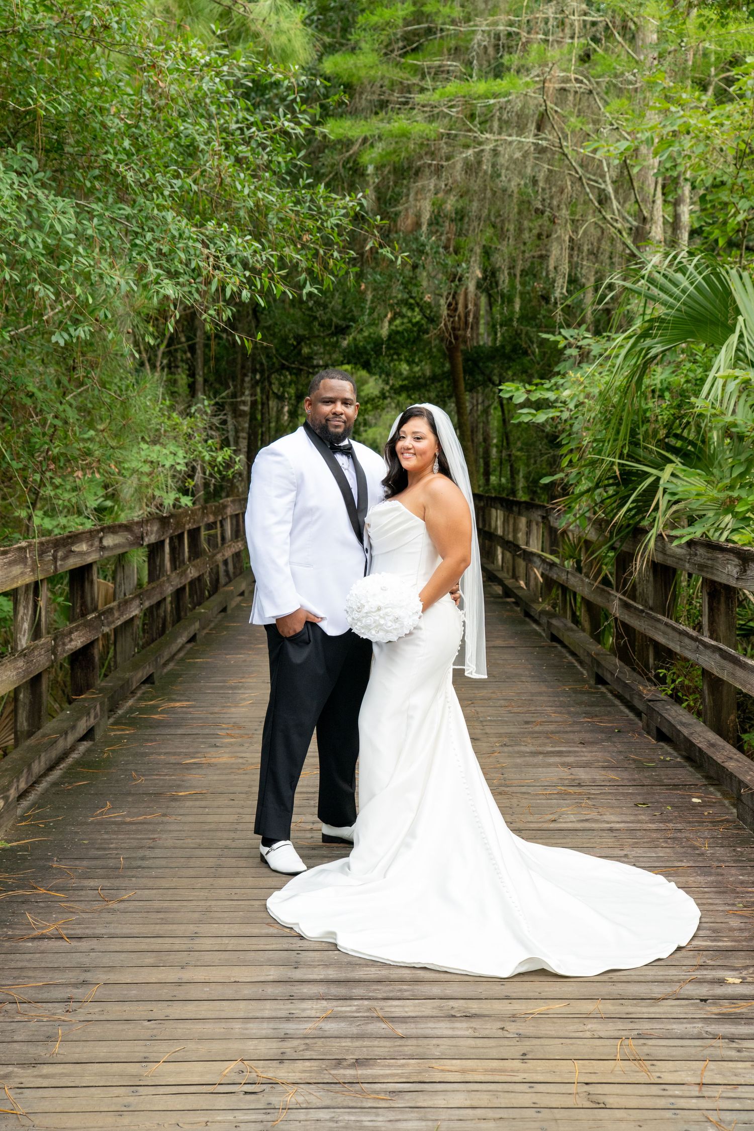 Bride and groom posing on a wooden bridge surrounded by lush greenery on their wedding day.