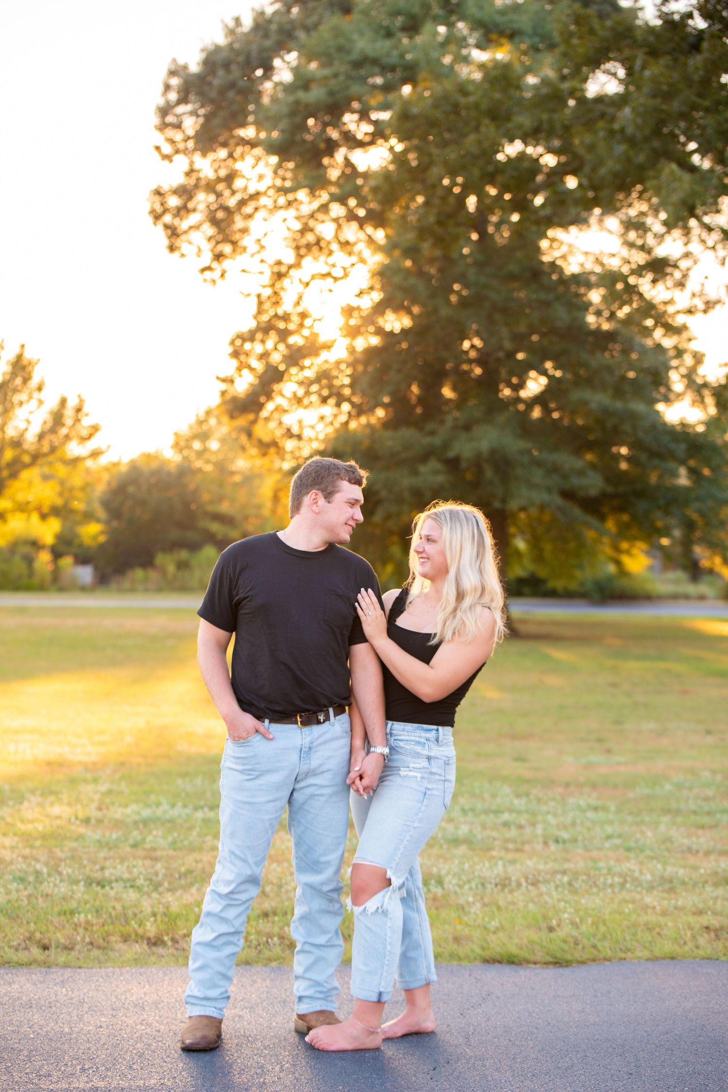 Couple holding hands smiling at each other during golden hour sunset in an open park setting.