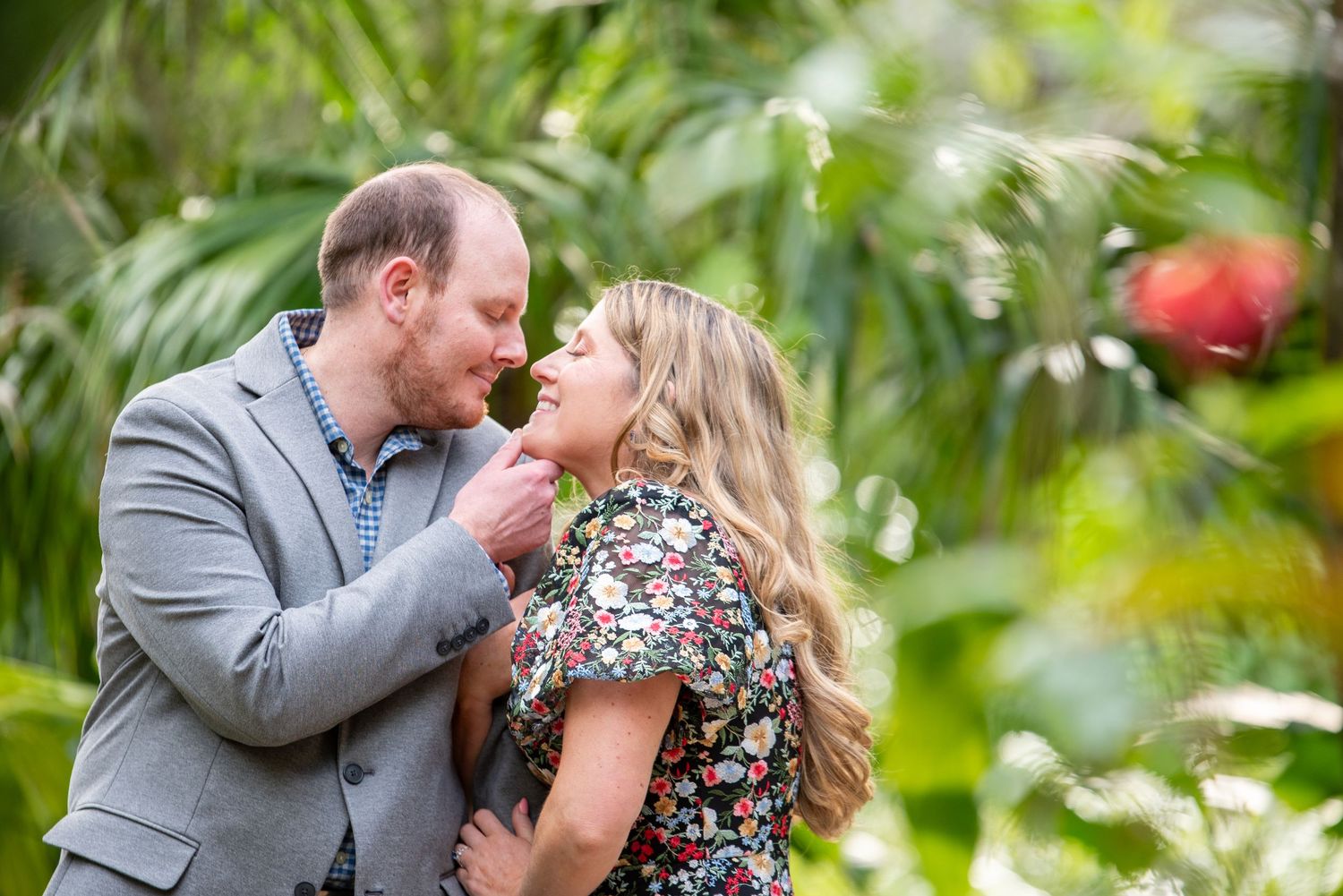 Couple shares a tender moment surrounded by lush tropical greenery during engagement shoot.
