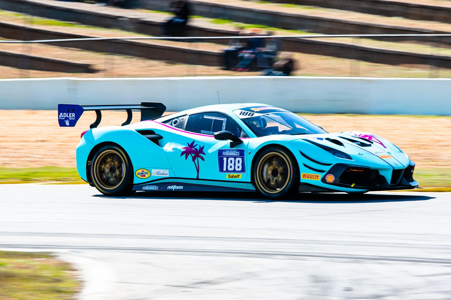 Teal Ferrari 488 GT3 race car number 188 with palm tree livery speeding on track.