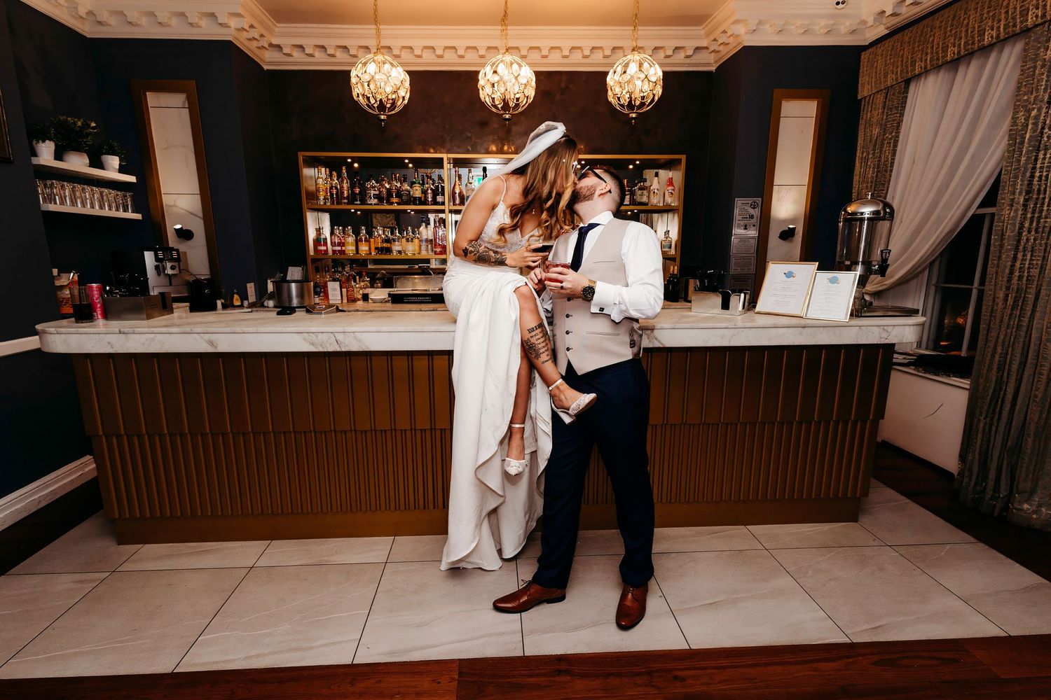 Bride sits on ornate panelled bar gently kissing groom, at The Old Palace Chester, elegant luxury wedding venue.