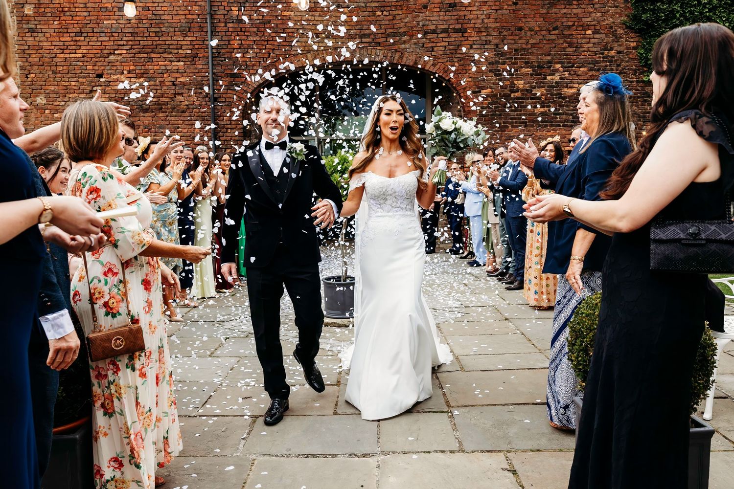 Wedding guests throw confetti as the newlyweds exit along a brick pathway at the Barn at Morley's Hall, Astley.  Manchester.