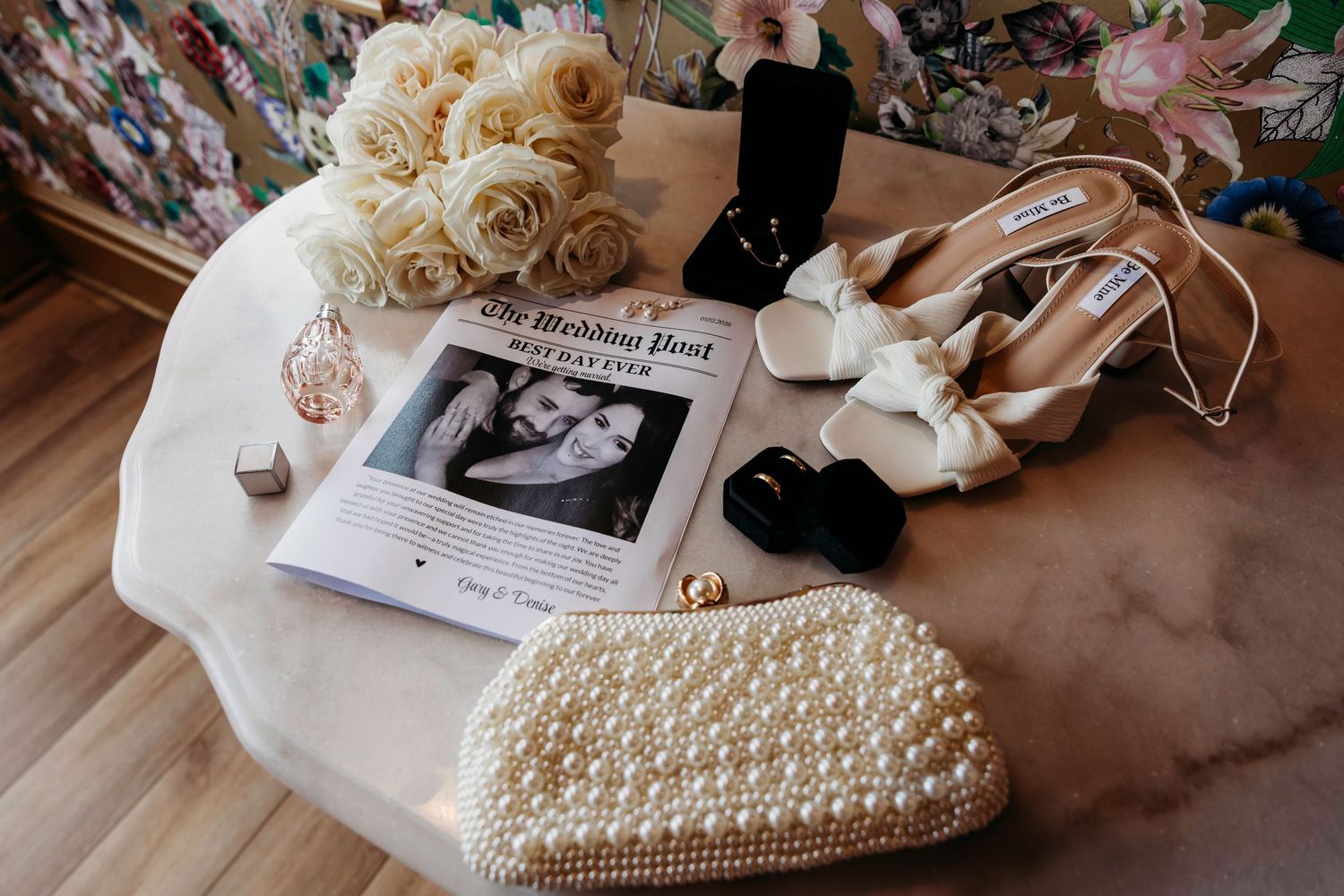 Wedding details flatlay with roses, pearl clutch, and wedding newspaper on marble surface at the Shankly Hotel, Liverpool.