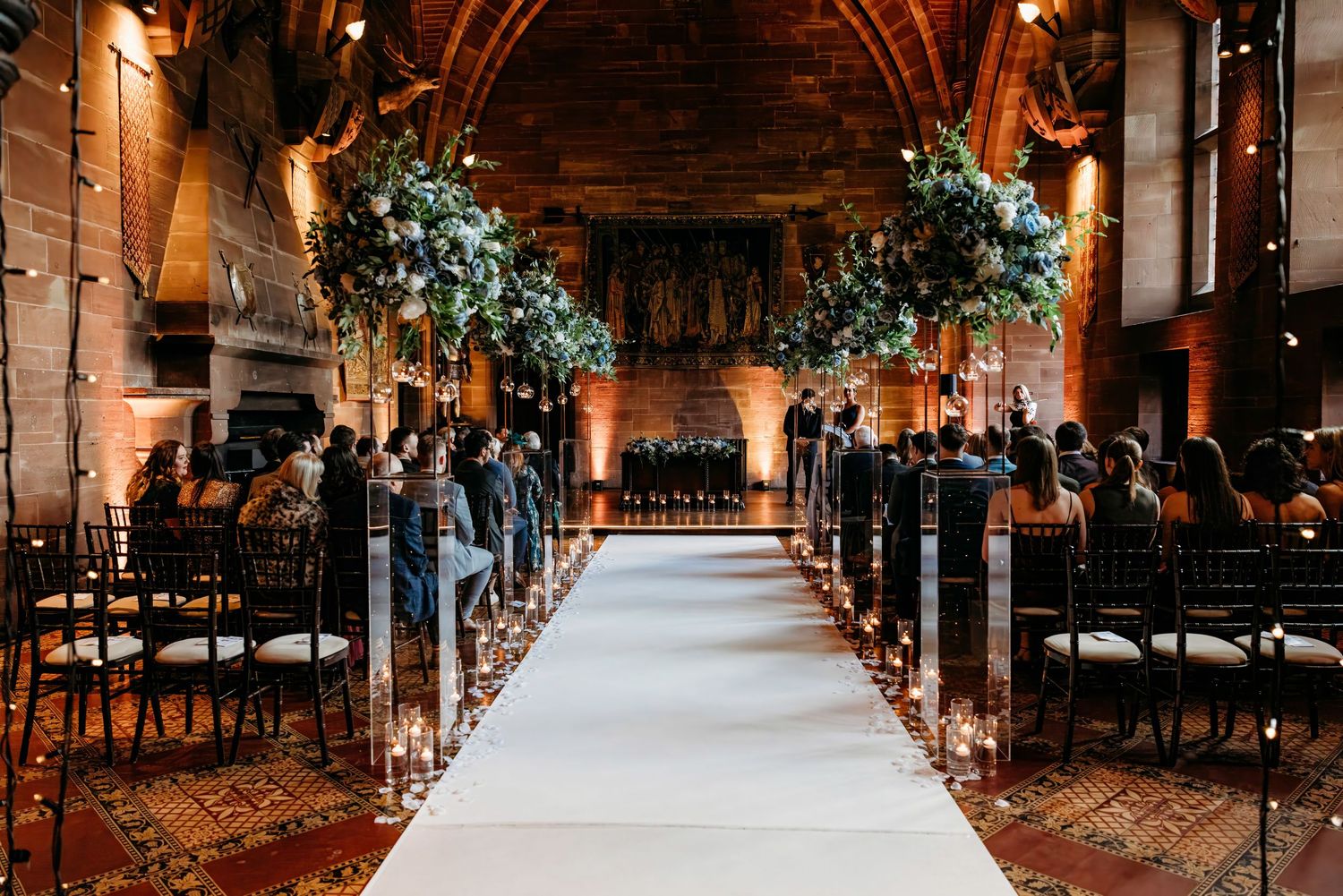 Elegant luxury wedding venue aisle decorated with floral arrangements and warm lighting.  Peckforton Castle, Cheshire.