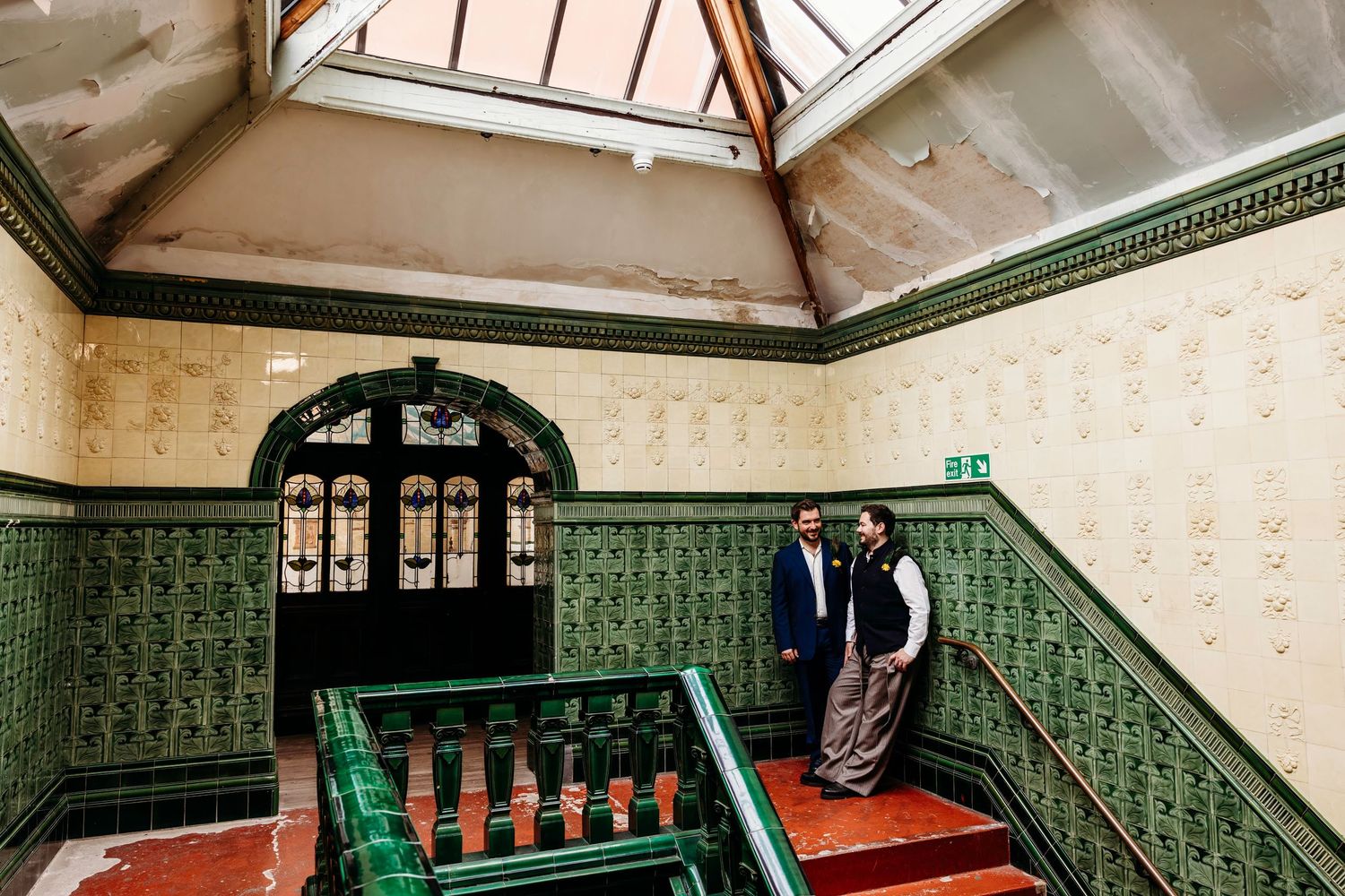 Ornate Victorian-era bathroom interior with green tile walls, stained glass windows and decorative archways.