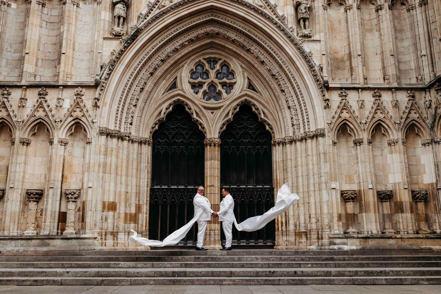 Wedding couple posing in front of York Minister, an ornate gothic cathedral entrance with flowing wedding sashes.