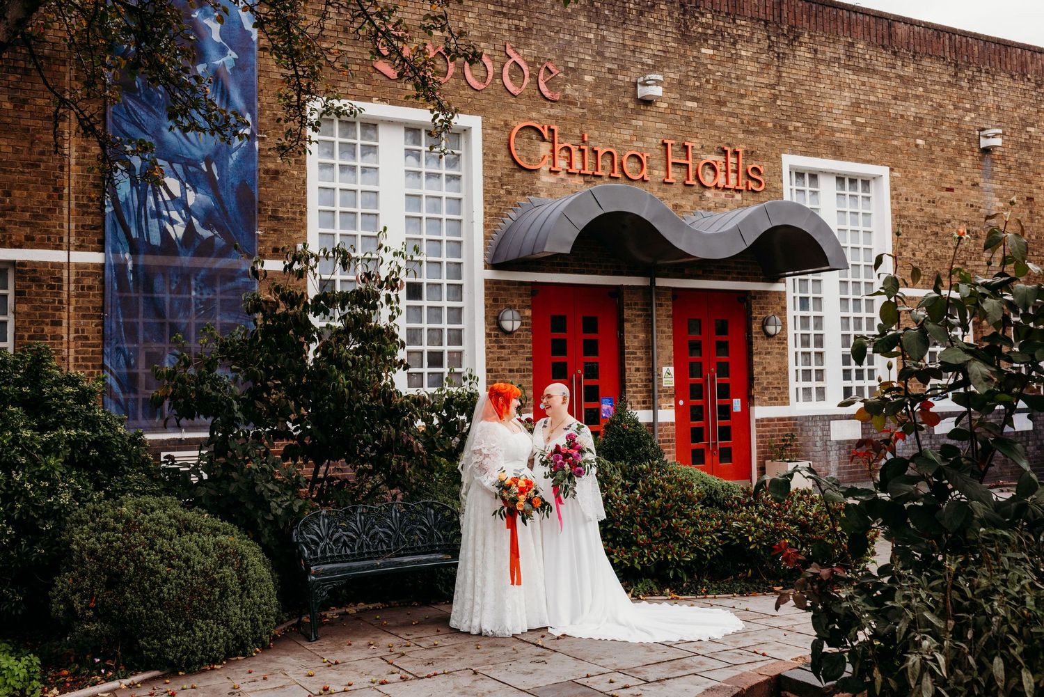 Two brides in white dresses standing outside Spode China Halls building after their beautifully intimate ceremony at Stoke Town Hall.