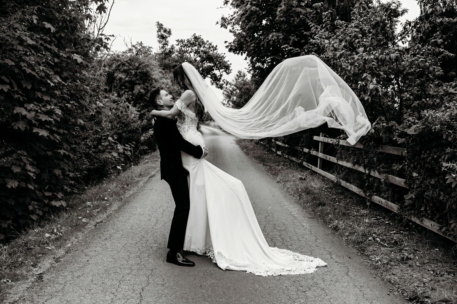 A romantic wedding couple shares intimate moments on a tree-lined path in black and white photography at the Barn at Morley's Hall, Astley.