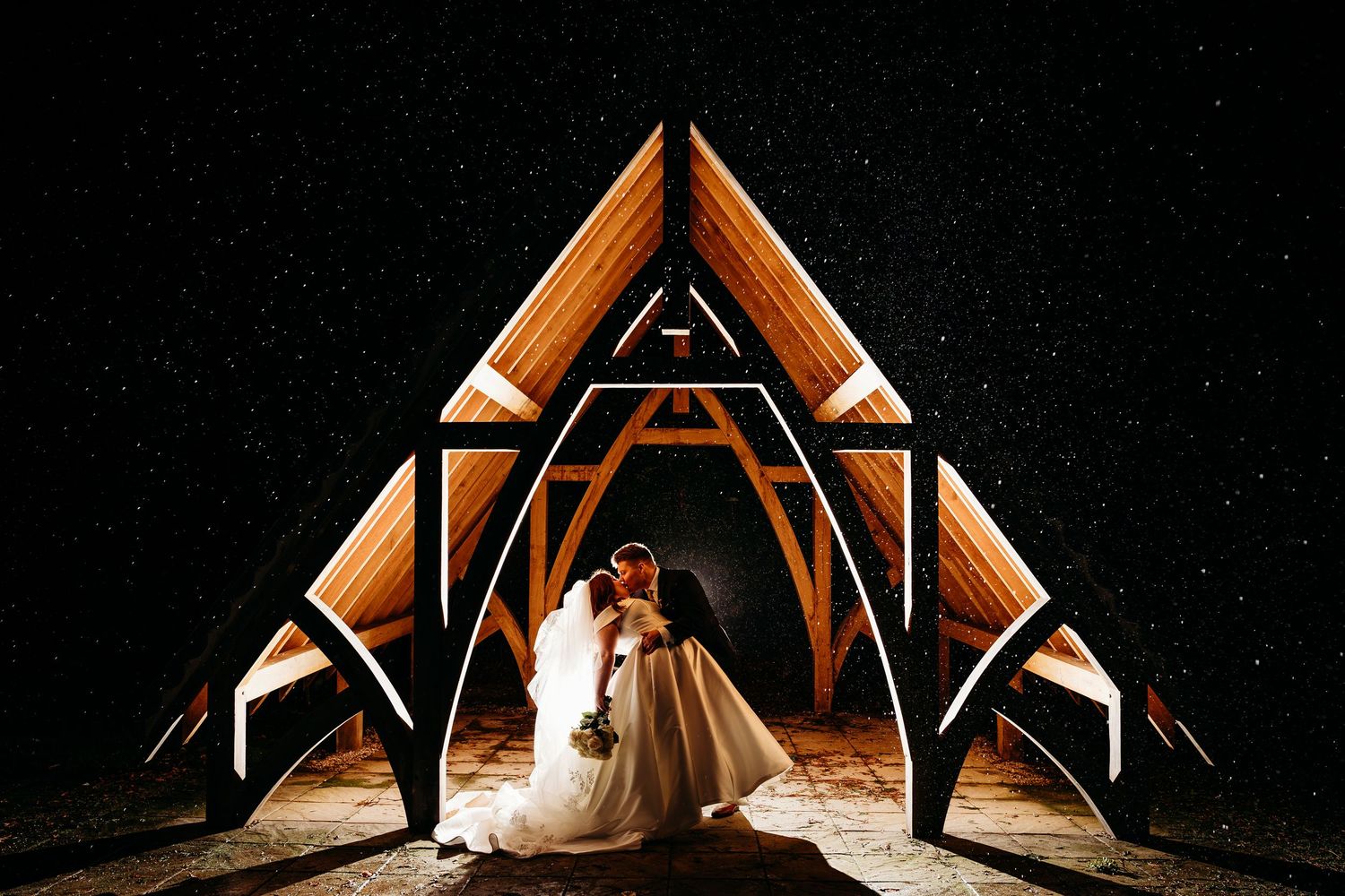 Bride and Groom dip and kiss in the night at Highfield Hall. Dramatic nighttime portrait with geometric lighting and architectural elements.