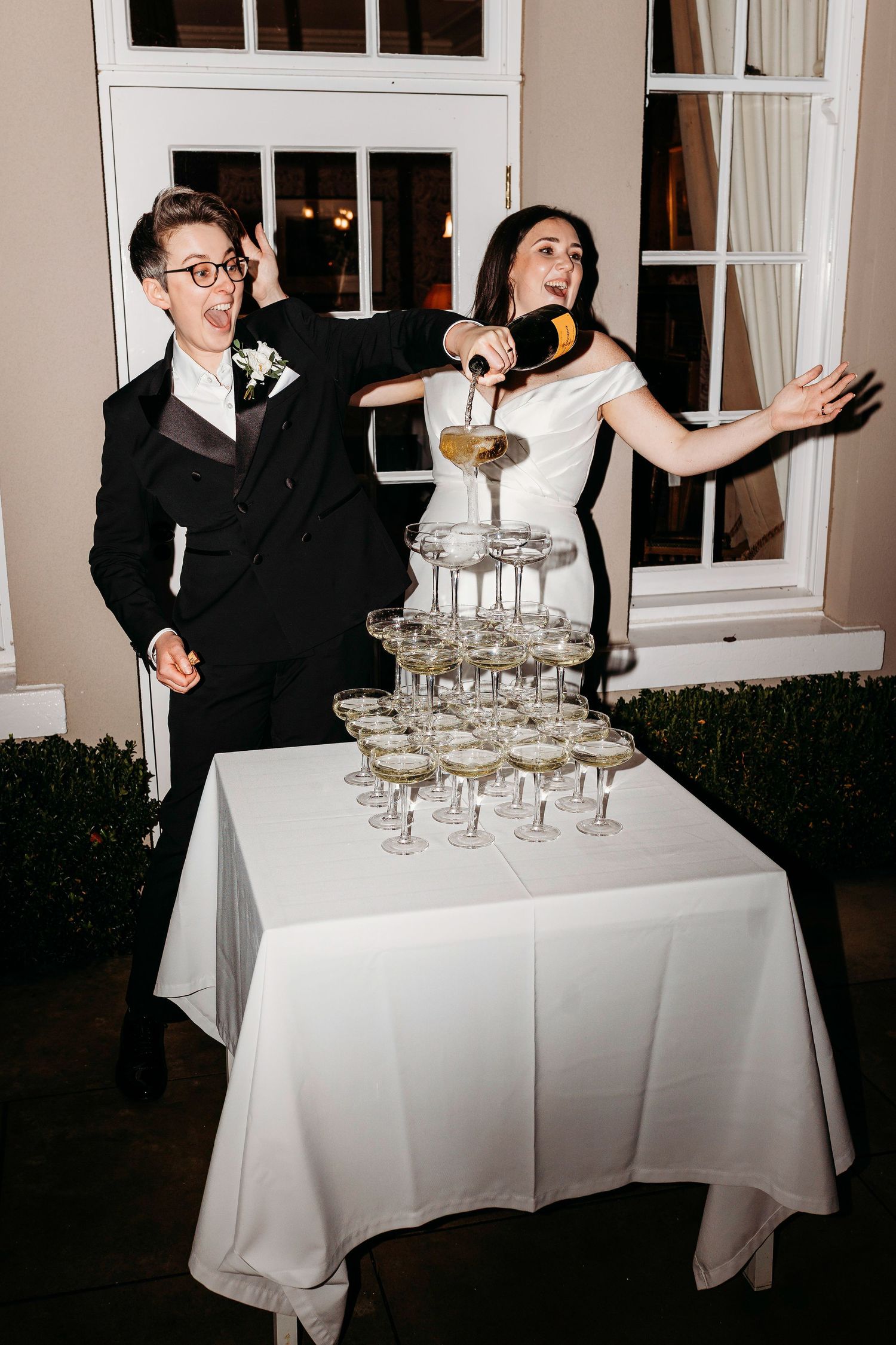 Wedding guests gather around an elegant champagne tower setup on white tablecloths at an outdoor reception at Burtonfields Hall, York.