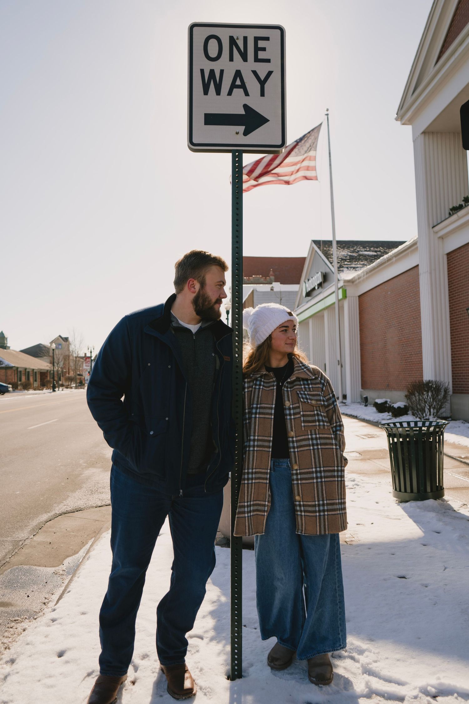 Winter street scene with people standing near a one-way sign in snowy conditions.