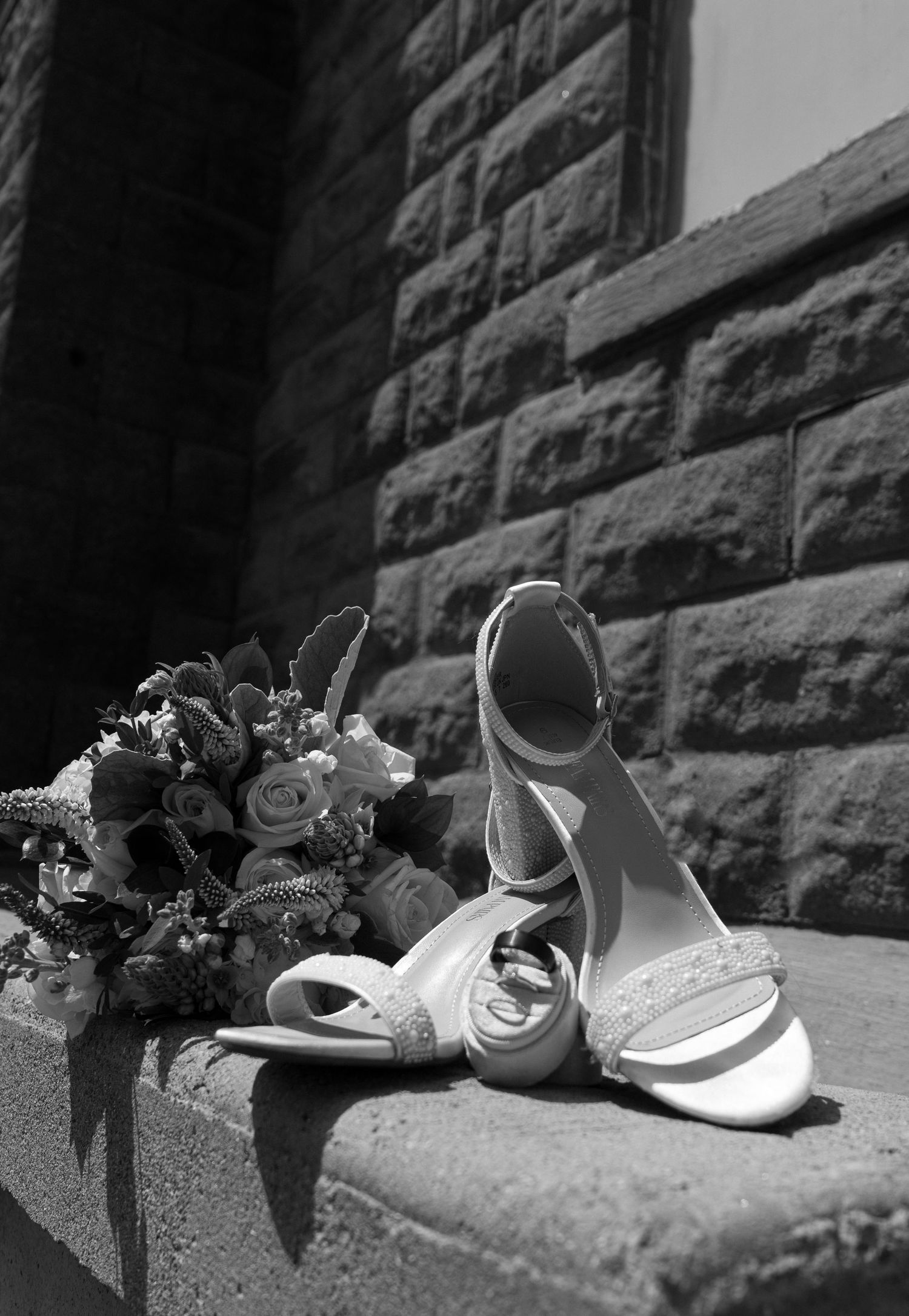 Black and white photo of elegant bridal shoes arranged on stone steps.
