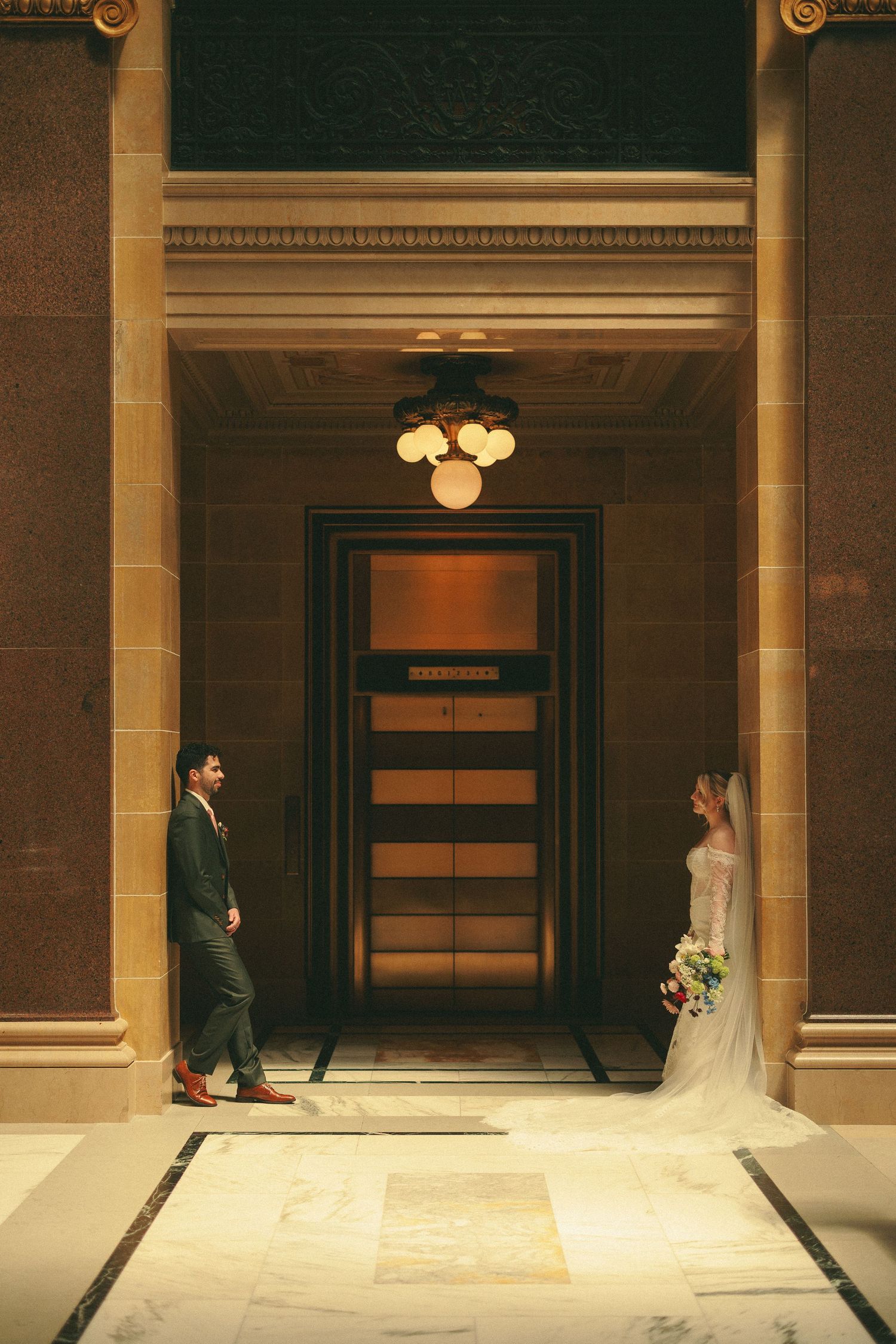 Wedding couple photographed in an elegant indoor hallway with warm lighting and architectural details.