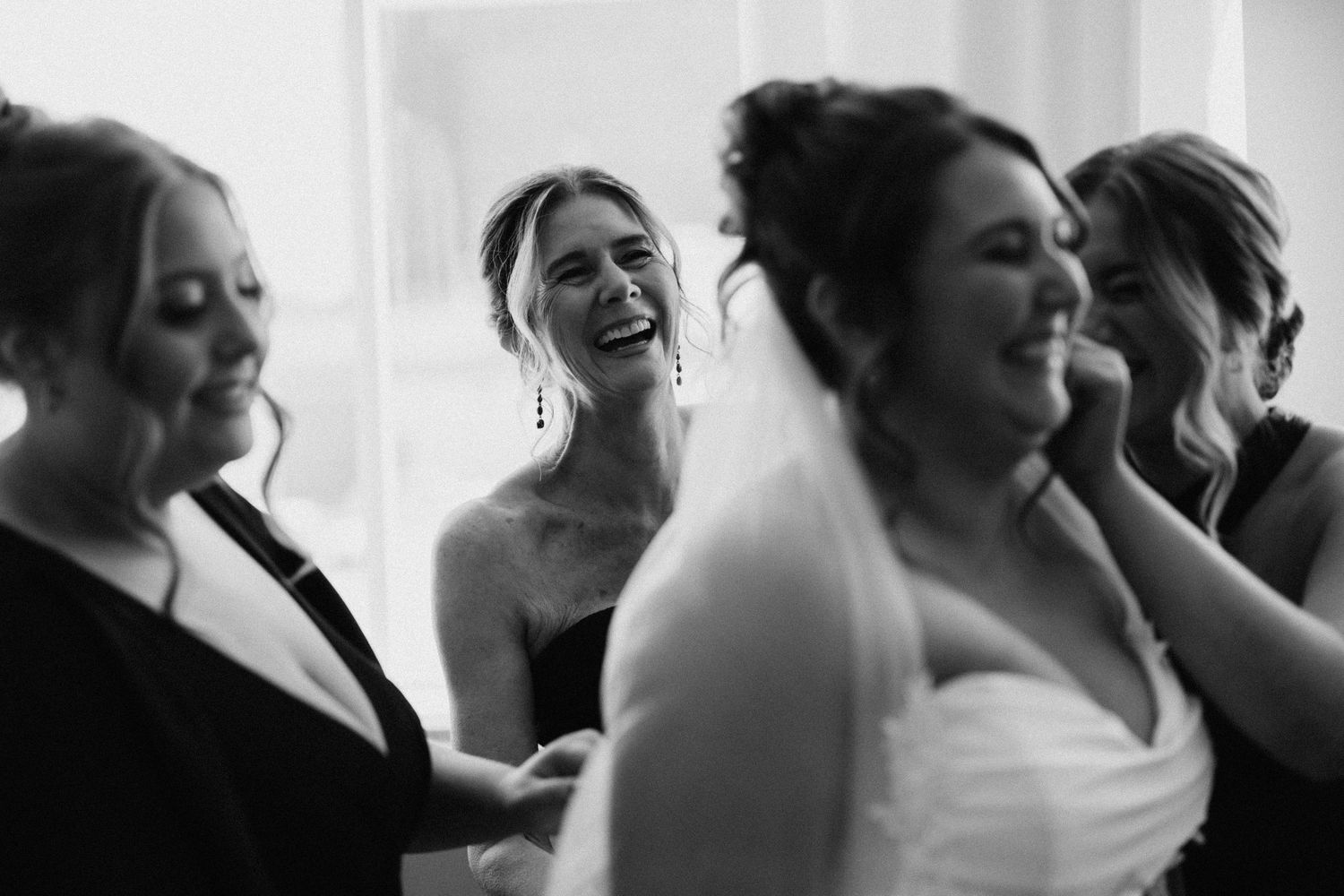 A group of wedding guests share joyful laughter during a candid black and white moment.
