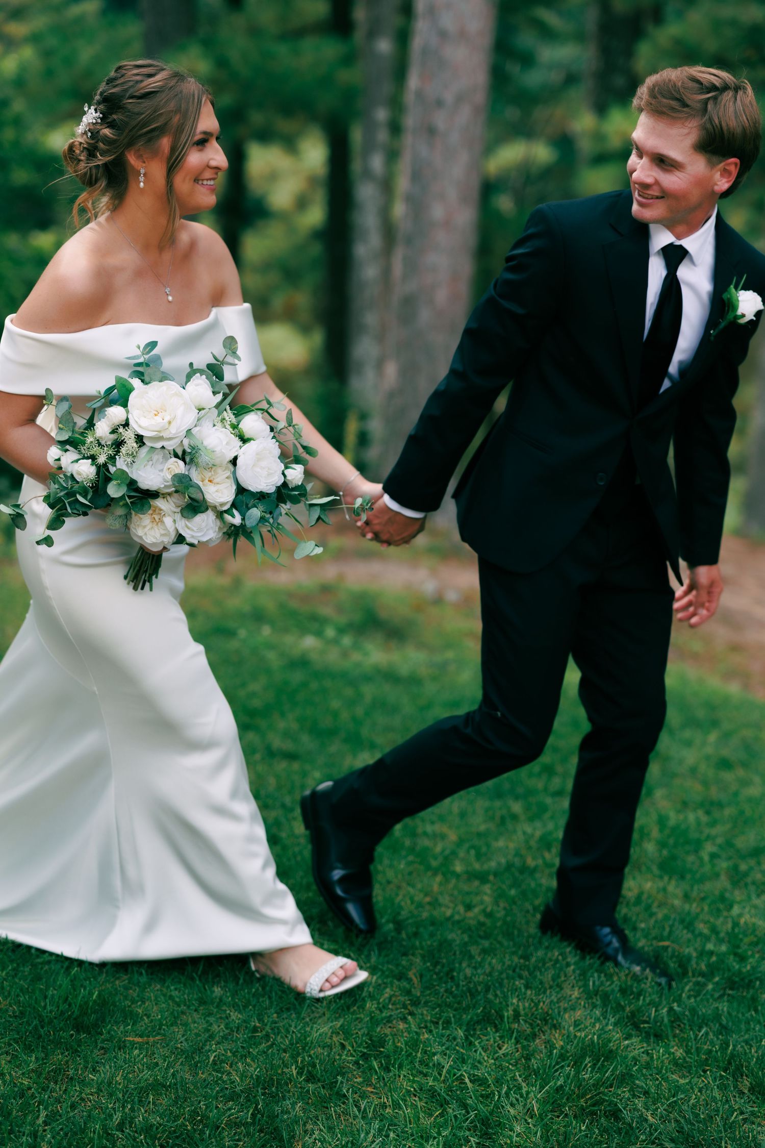 Playful wedding photos on grass showing white dress and black suit details.