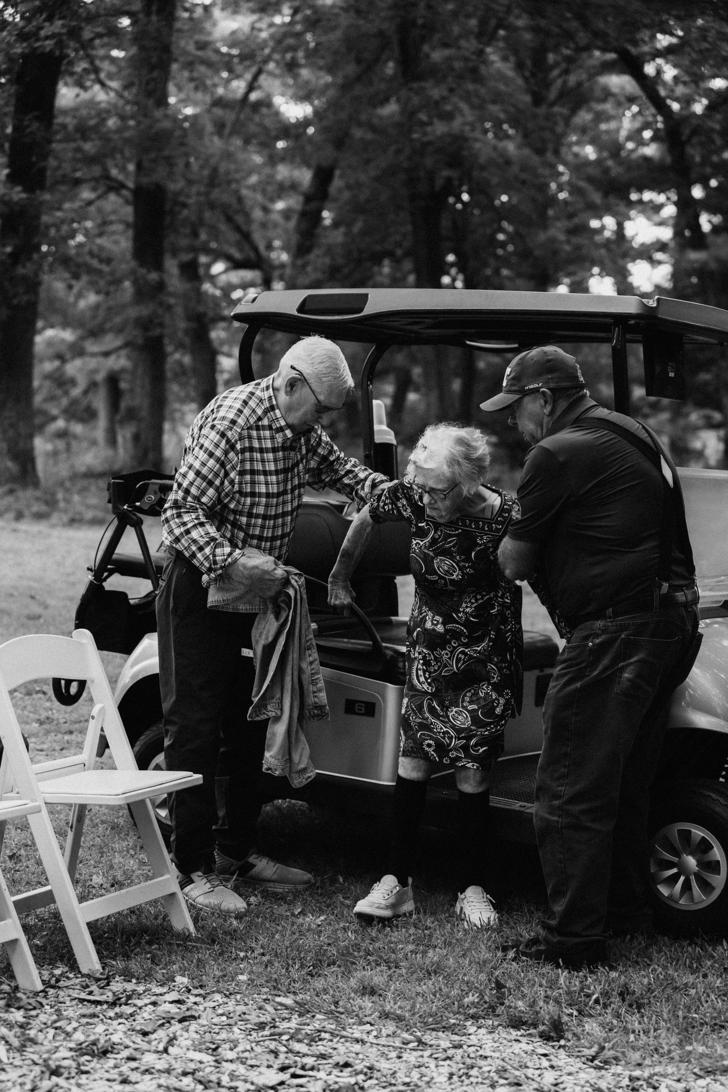 Wedding guests gather around a car trunk in a casual outdoor setting.
