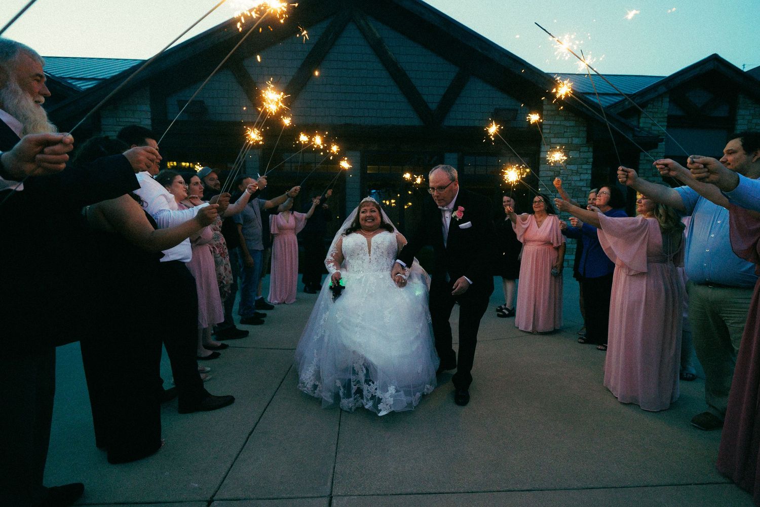 Wedding party dances together at reception with pink bridesmaids dresses and string lights overhead.