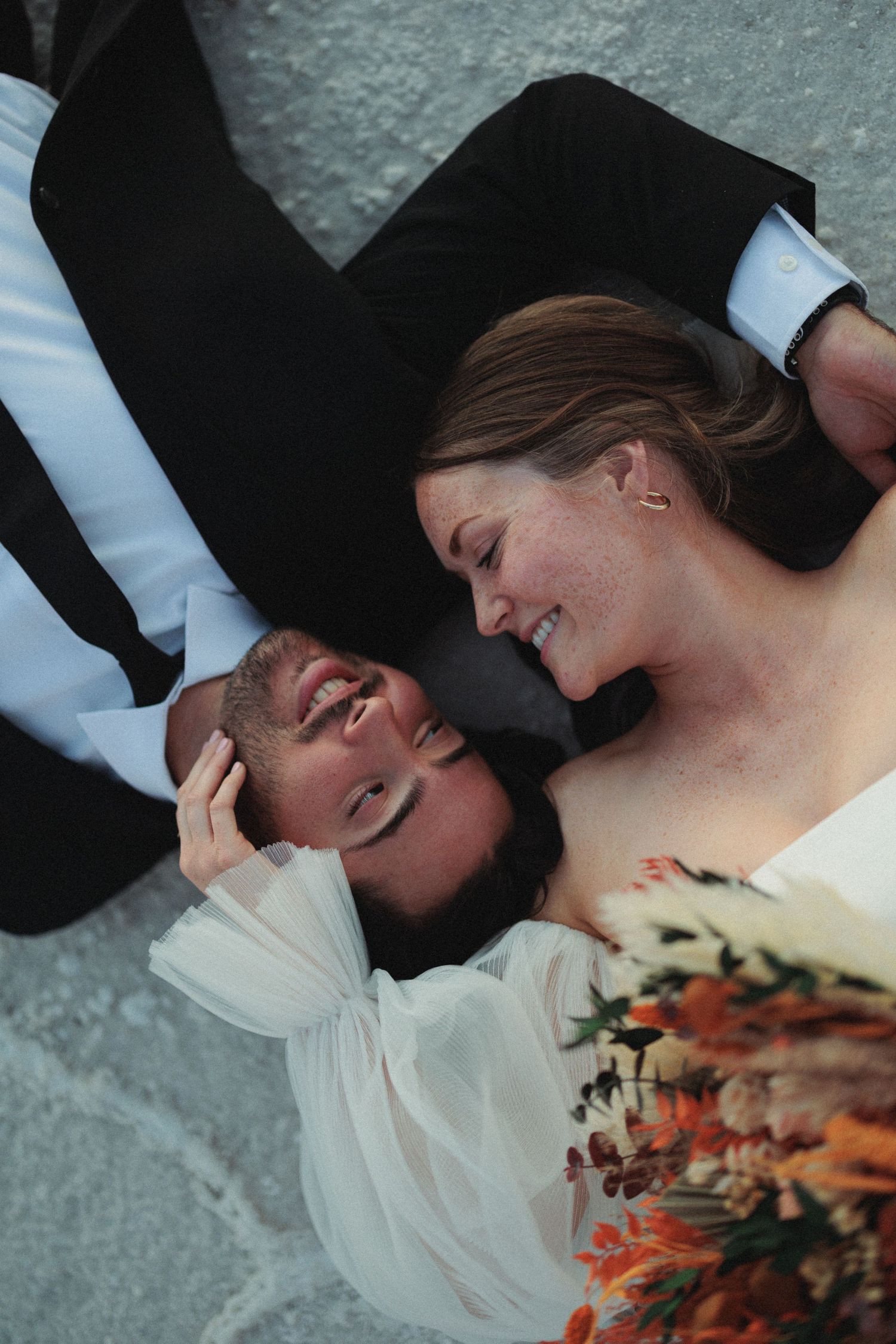 Couple lying on utah salt flats with bridal bouquet during intimate wedding photoshoot.