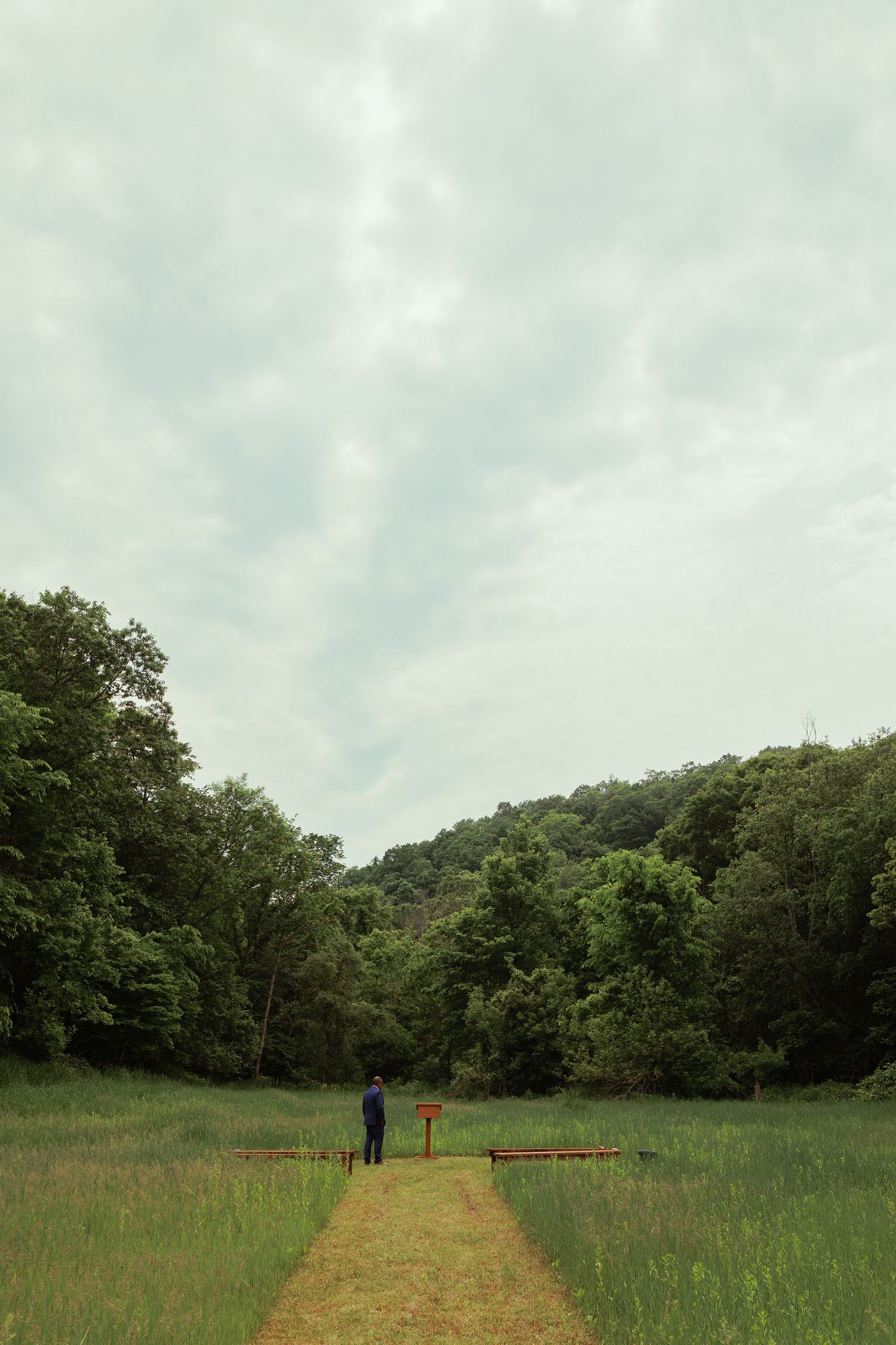 A scenic grassy meadow path leads through green trees under cloudy skies.