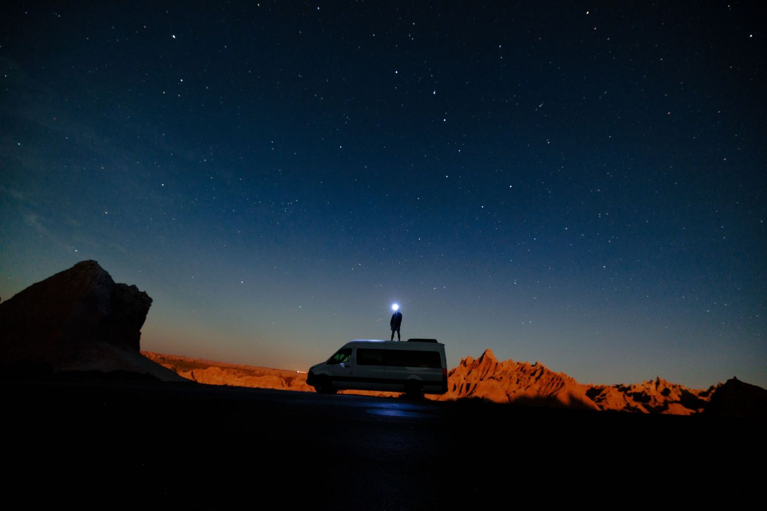 Night sky over mountain landscape with silhouetted figure and flashlight beam.