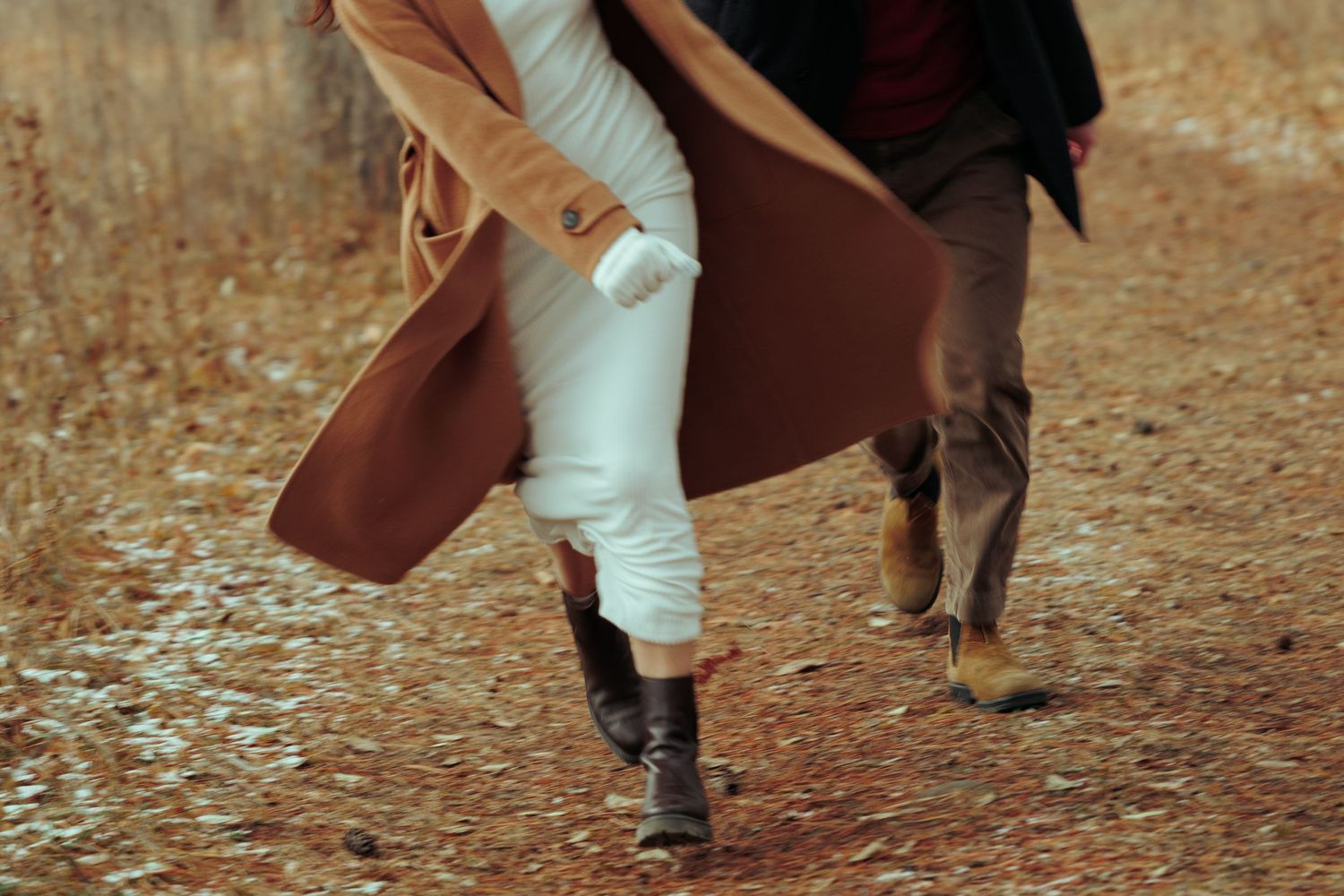 Two people walking through fallen leaves on an autumn path.