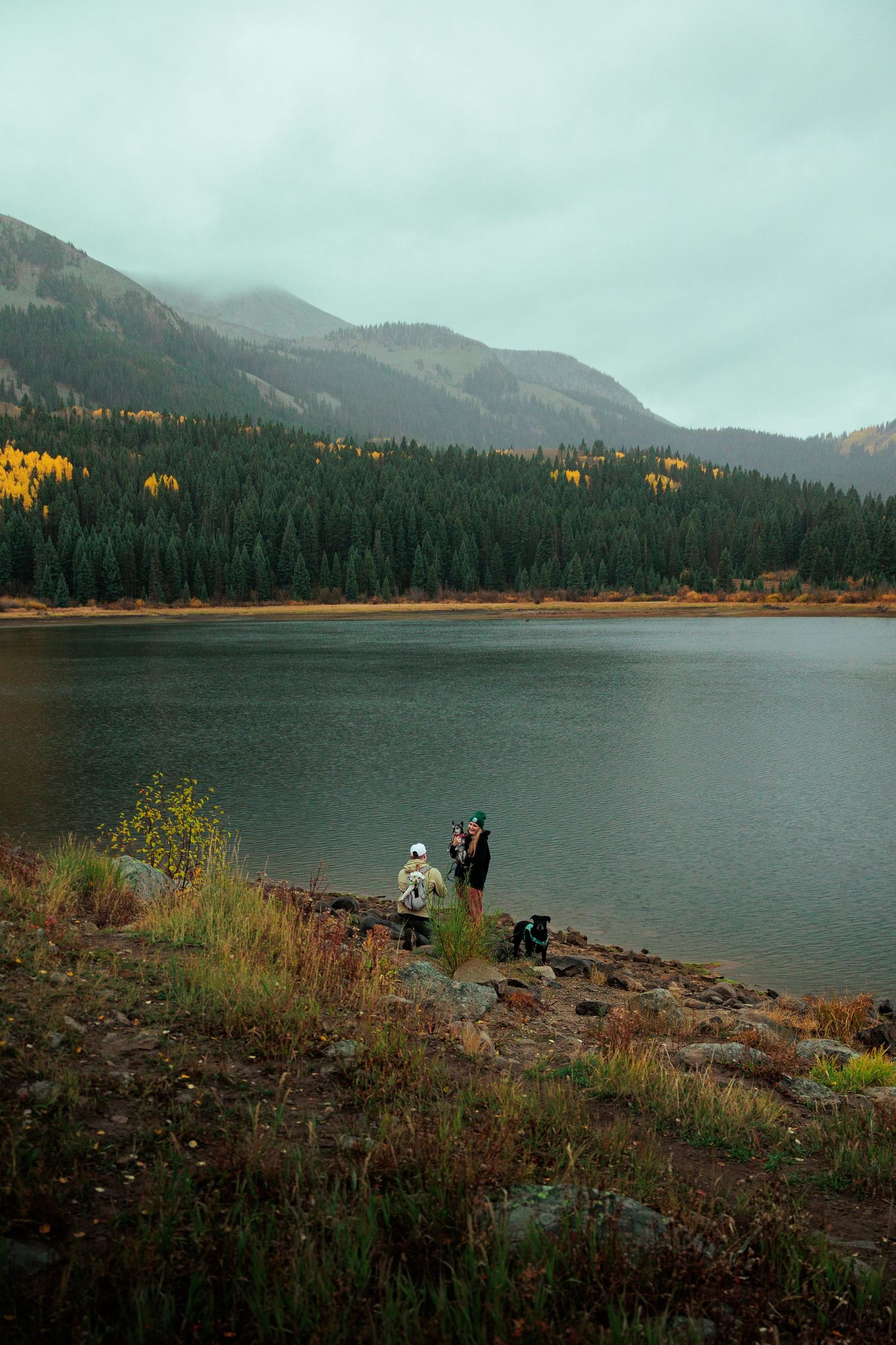 Mountain lake surrounded by fall foliage and evergreen forests under cloudy skies.