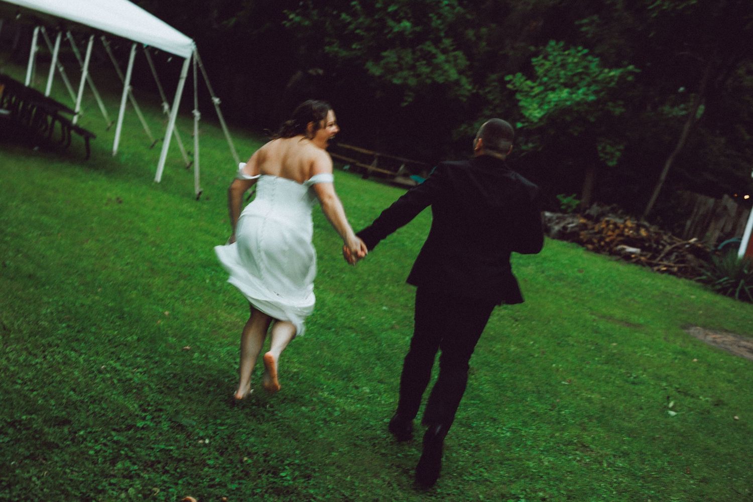A couple dances on grass during a wedding celebration with trees in the background.