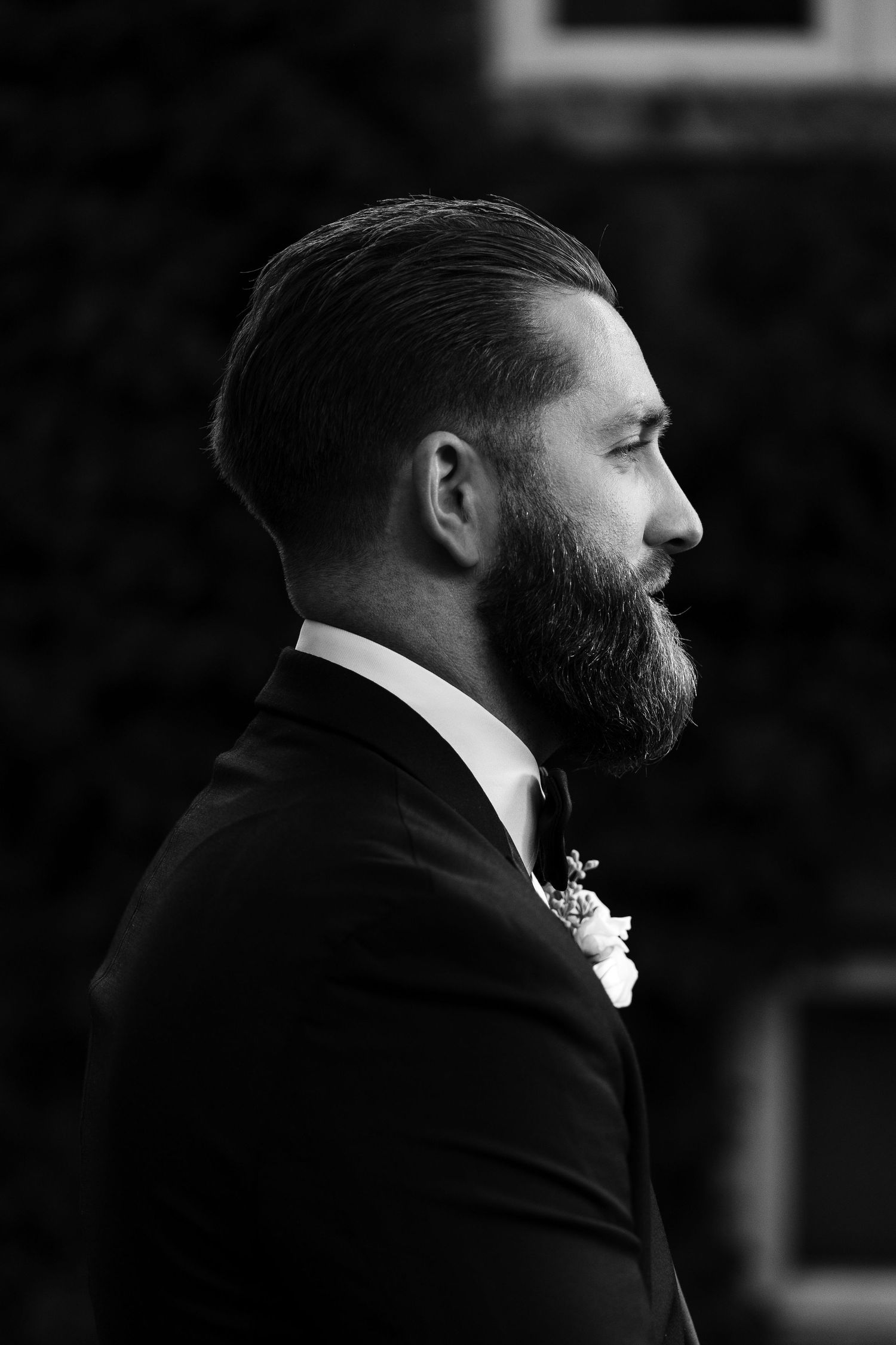 Profile view of bearded person in formal attire shown in dramatic black and white.